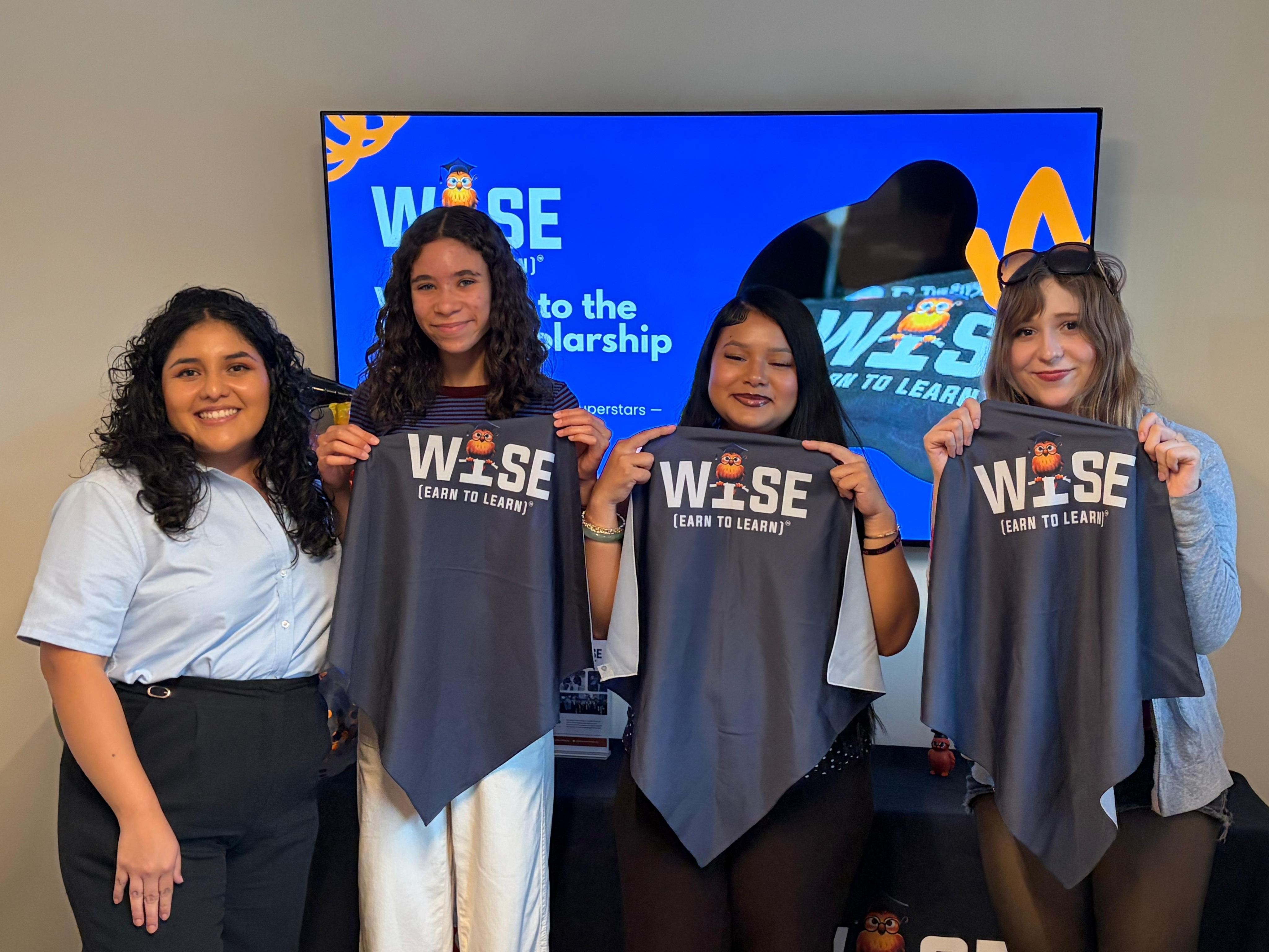 A group at the Altadena Girls orientation displays WISE shirts beside a program screen.